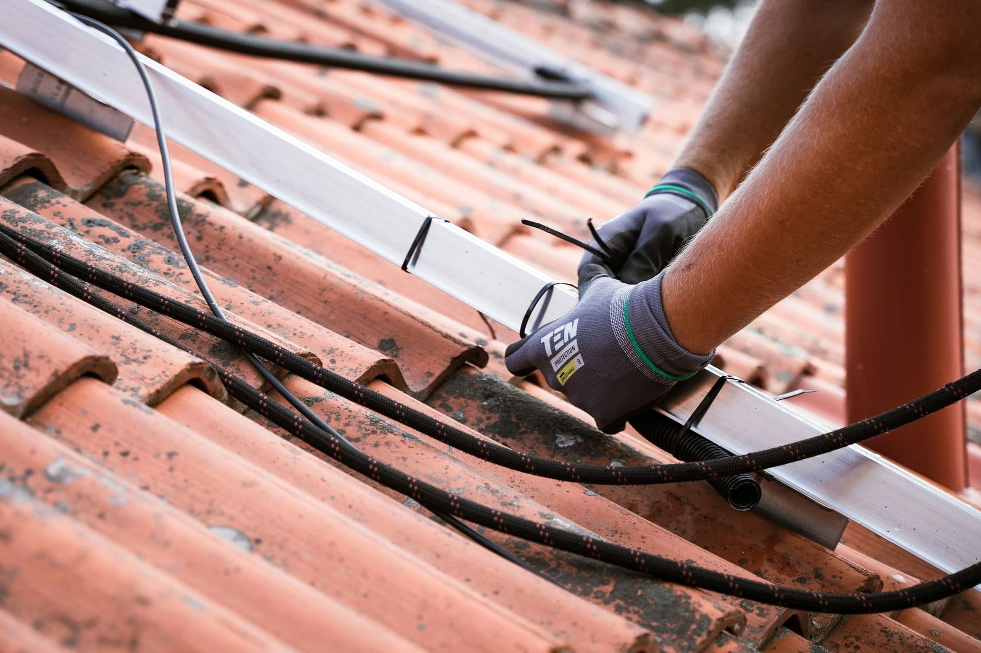 Installateur posant proprement les câbles solaires le long d'un toit en tuiles