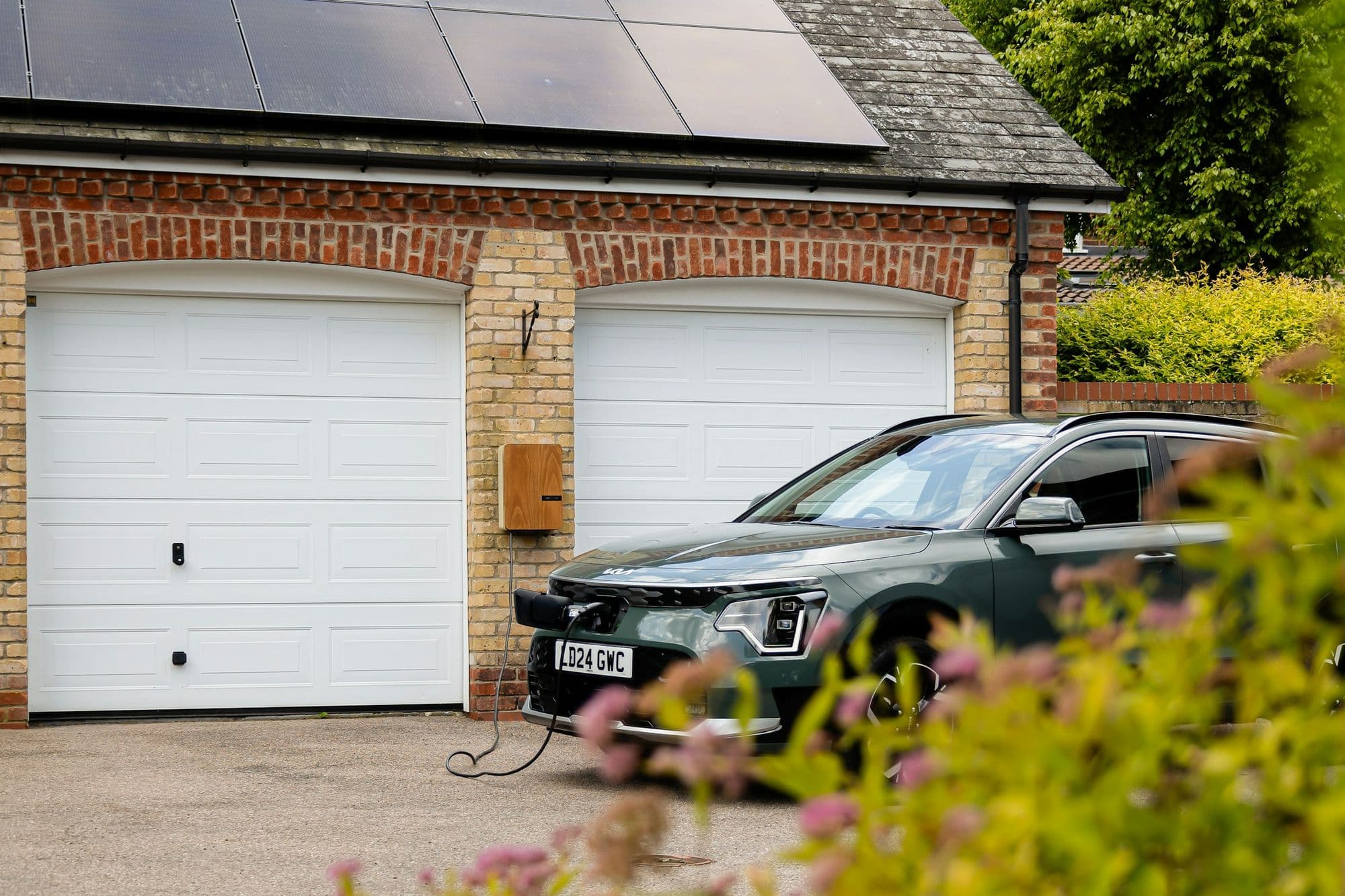 Electric car charging at a brick house with solar panels on the roof
