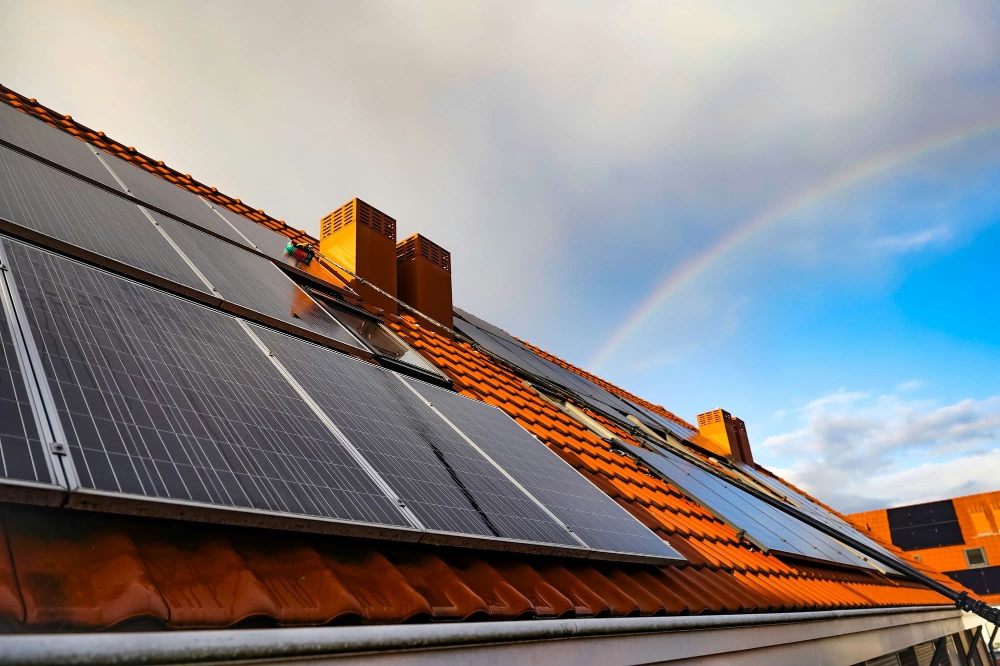 Solar panels on a red tiled roof, with a rainbow in the sky