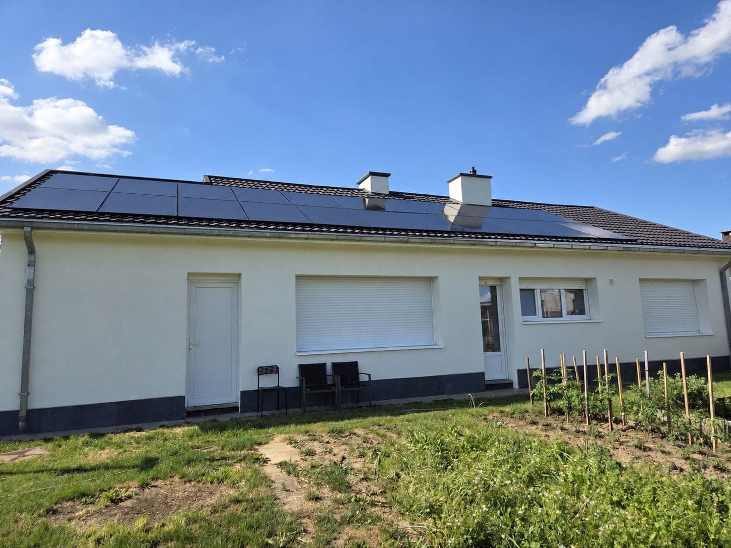 Maison blanche de plain-pied vue du jardin, avec des rangées de panneaux solaires full black sur son toit en tuiles et deux cheminées