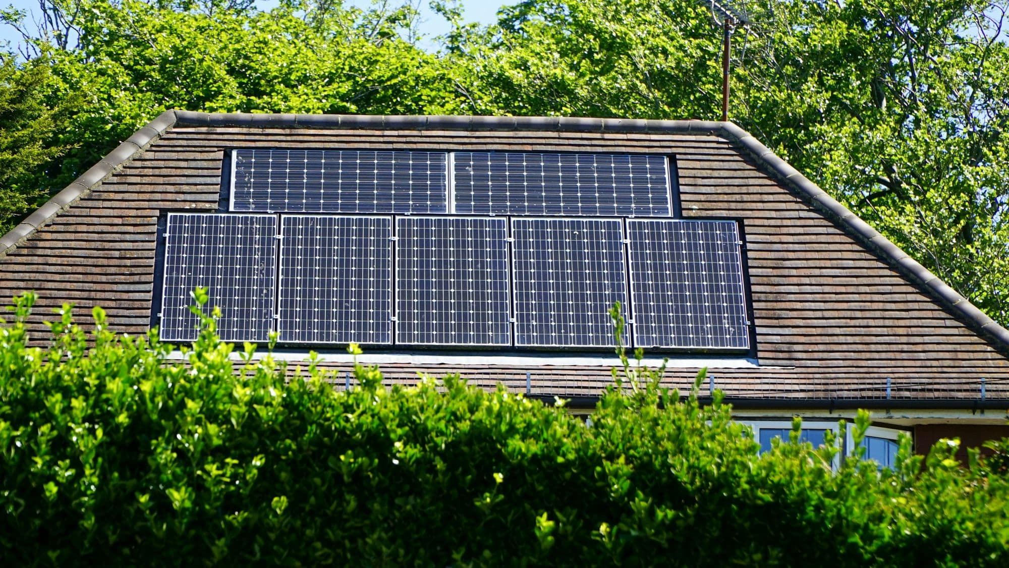 Panneaux solaires noirs sur un toit en tuiles, derrière une haie